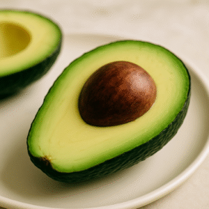 A digital photograph showcases a halved avocado with its seed intact, resting on an off-white ceramic plate.