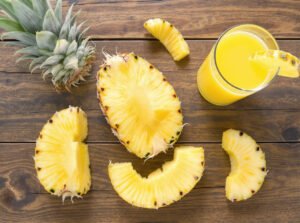 Fresh pineapple slices and juice next to prunes and kiwis on a fiber-rich breakfast table.